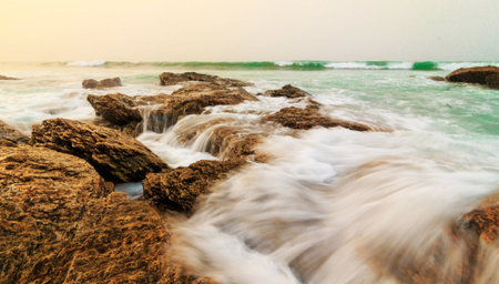 Beautiful tropical beach with sea waves crashing on the rocks at sunsetの写真素材