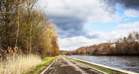 Autumn landscape with a road on the river bank and cloudy sky