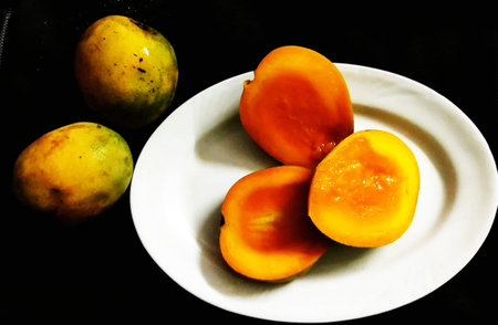 Ripe mango fruits on a white plate on a black background.