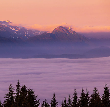Sunrise in the mountains with clouds and fog in the foreground.