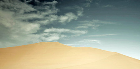 Desert sand dunes with blue sky and white clouds in the backgroundの写真素材