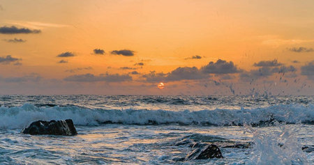 Sunset on the sea with waves breaking on the rocks and splashesの写真素材
