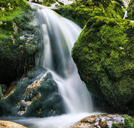 Waterfall on a mountain river with green moss and rocks in summerの写真素材