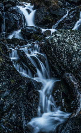 Long exposure of a small waterfall flowing through rocks in the mountains.