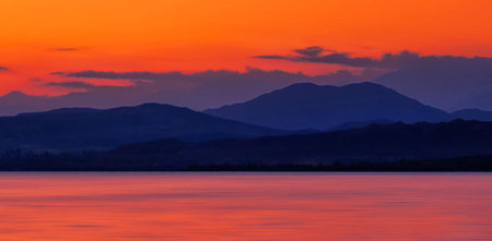 Sunset on the lake with mountains in the background and orange sky