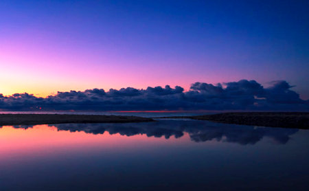 Sunset over the sea with clouds reflected in the calm water.の写真素材