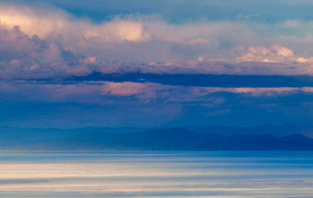 Sunset over the sea with clouds and mountains in the background.