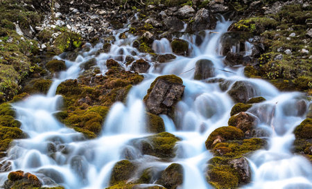 Waterfall in the mountains with moss and rocks in the foreground.