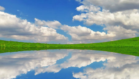 Green field and blue sky with white clouds reflected in water surface.の写真素材