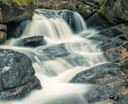 Long exposure of a waterfall flowing over rocks in the woods in autumn