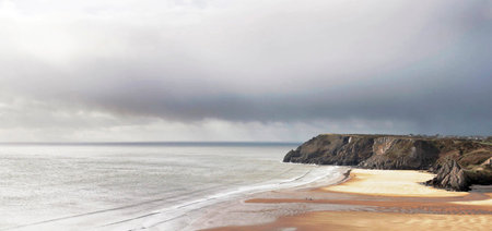 A panoramic shot of a beach in Cornwall under a cloudy sky