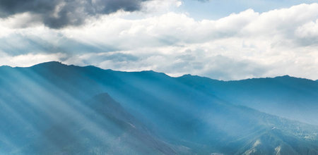 Sun rays through the clouds over the mountains. Panoramic view.