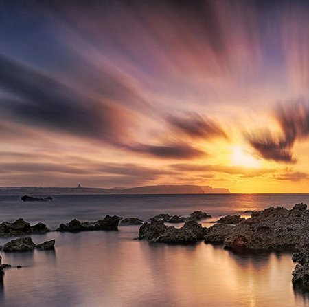 Beautiful sunset over the sea with rocks in the foreground and a dramatic sky