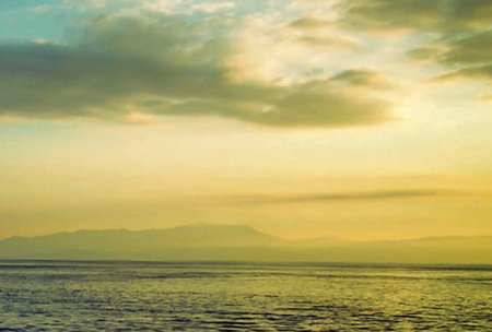 Sunset over the sea with mountains on the horizon and cloudy skyの写真素材