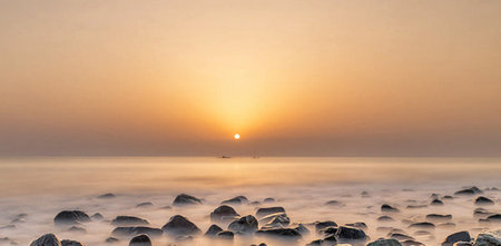Sunset over the sea with stones in the foreground, long exposure