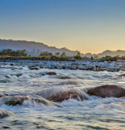 Sunset over a mountain river with clear water and rocks on the foregroundの写真素材