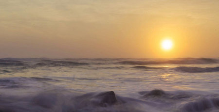 Sunset over the sea with waves crashing on the rocks and splashing waterの写真素材