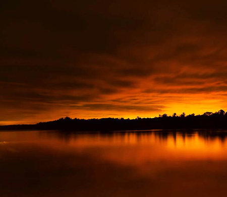 Beautiful sunset over the lake with reflection of trees and clouds.の写真素材