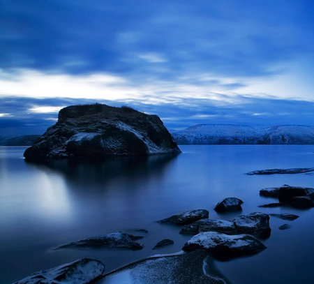 Long exposure shot of a rocky beach at dusk with mountains in the backgroundの写真素材