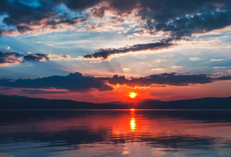 Sunset over the lake with clouds and mountains in the background.の写真素材