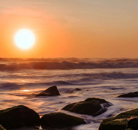 Beautiful sunset over the sea with rocks in the foreground and orange sky
