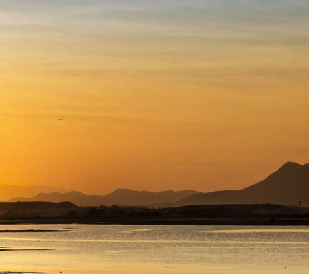 Sunset over the sea with silhouettes of mountains in the backgroundの写真素材