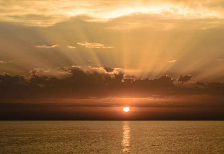Sunset over the sea with sun rays in the sky and cloudsの写真素材