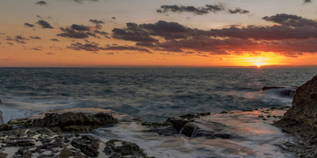 Sunset over the sea with waves and rocks in the foreground.の写真素材