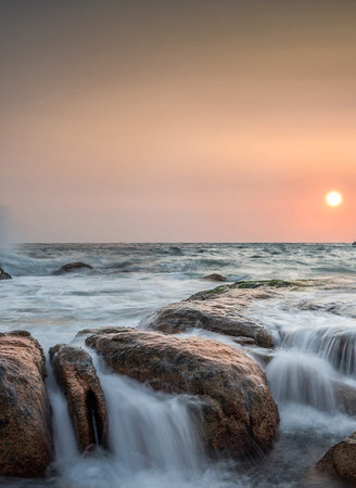 Beautiful sunset at the beach with rock and wave in the seaの写真素材