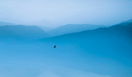Bird flying in the blue sky with mountains in the backgroundの写真素材
