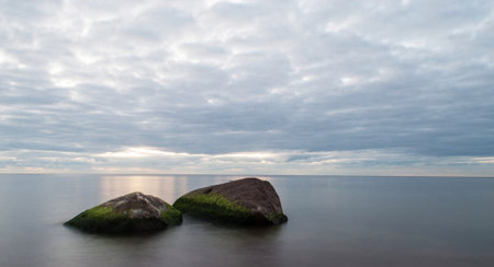 Long exposure of two stones in the sea with a cloudy sky.の写真素材