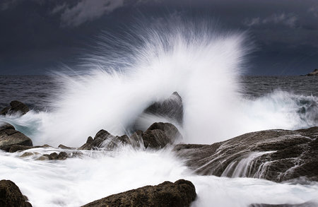 Stormy waves crashing on the rocks and forming a spray effect.