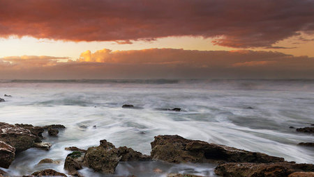 Beautiful sunset at the beach with waves breaking on the rocks.