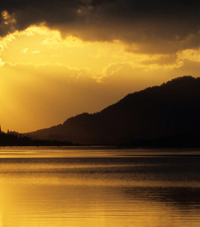 Sunset on the lake with mountains silhouettes and clouds in the backgroundの写真素材