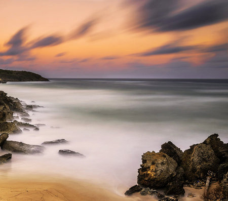 Long exposure of a beach at sunset with rocks in the foreground, long exposure