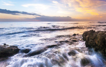 Beautiful sunset on the beach with waves crashing against the rocks.