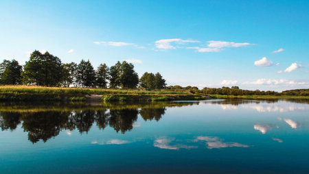 Landscape with the image of a lake, trees and blue sky
