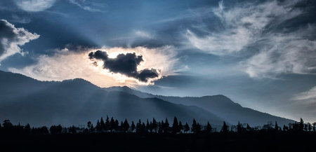 Sunset in the mountains with silhouettes of trees and clouds.