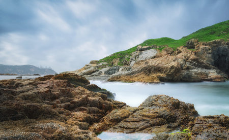 Tropical beach with rocks and green grass under cloudy sky.の写真素材
