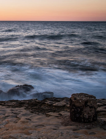 Sunset over the sea with rocks and water splashes in the foreground
