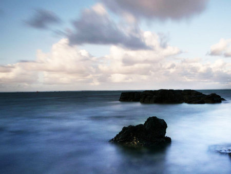 Long exposure of a rock in the middle of the ocean with cloudsの写真素材