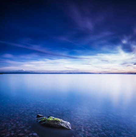 Long exposure shot of a lake with rocks in the foreground and cloudy skyの写真素材