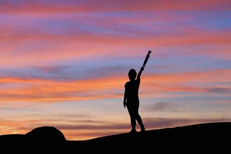 Silhouette of woman lifting tripod under the sky at sunsetの写真素材