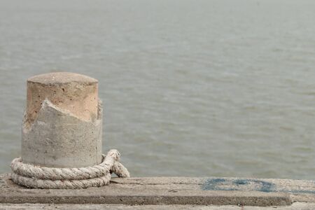Stone bollard with rope on boat dock and sea.