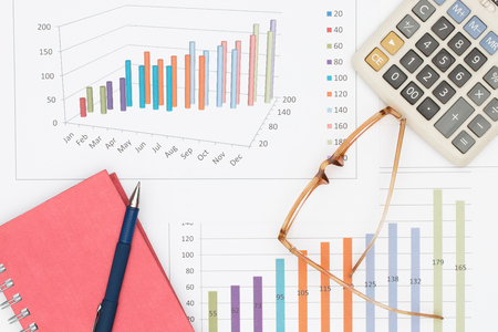 Business concept : Pen placed on notebook with glasses and calculator on graph background.の写真素材