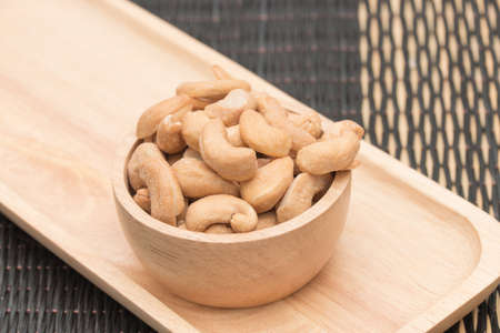 Cashew nuts in the wooden cup placed on the wooden tray.の写真素材