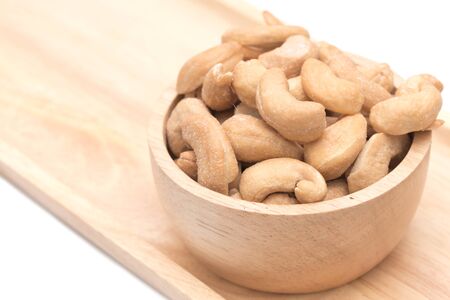 Cashew nuts in the wooden cup placed on the wooden tray on white background.の写真素材