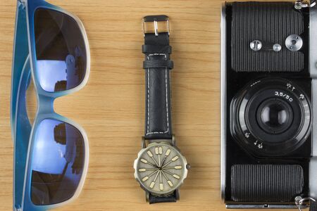 Top view of accessory: sunglasses, wristwatch, and camera on wooden floor.の写真素材