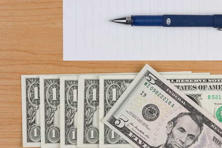 Dollars bills, note paper and pen on wood table.の写真素材