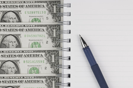 pen on notebook with dollars bills.